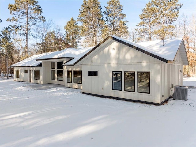 snow covered property featuring board and batten siding and central AC