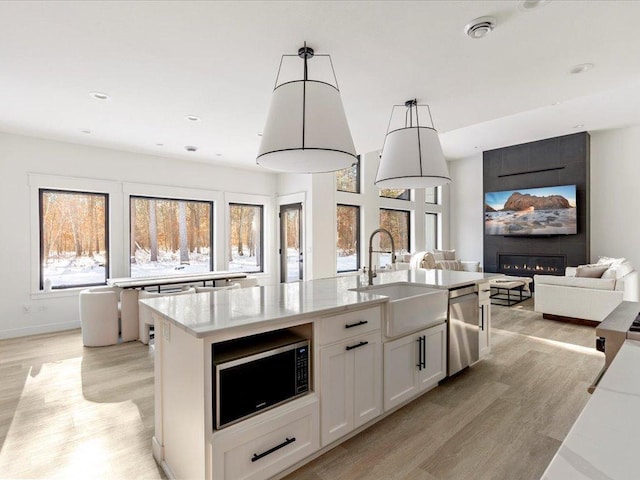 kitchen with light wood-style flooring, a kitchen island with sink, built in microwave, dishwasher, and a large fireplace