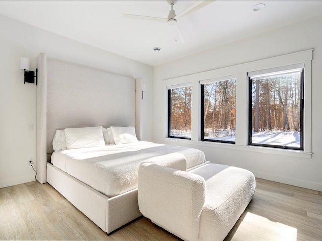 bedroom featuring light wood-type flooring, multiple windows, baseboards, and ceiling fan