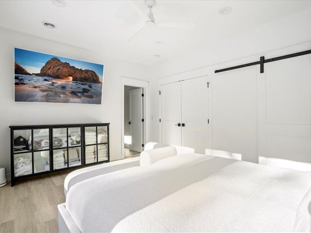 bedroom featuring ceiling fan, a barn door, visible vents, and wood finished floors