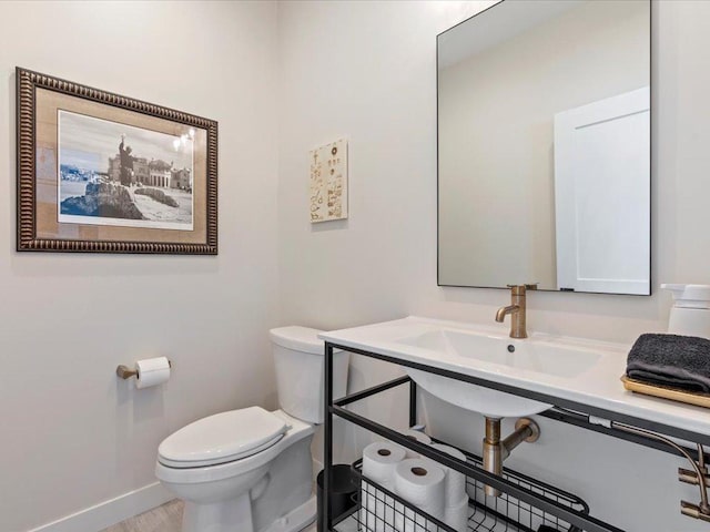 half bath featuring toilet, wood finished floors, baseboards, and a sink