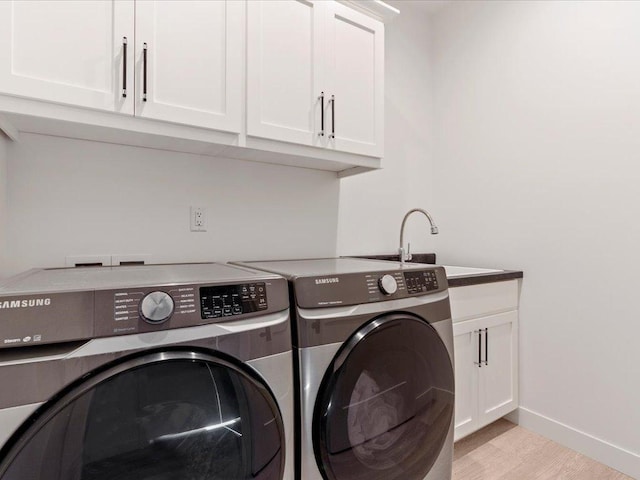 laundry room featuring baseboards, light wood-style flooring, cabinet space, a sink, and washer and clothes dryer