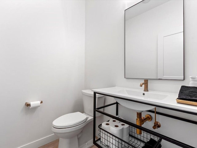 half bath with a sink, baseboards, toilet, and wood finished floors