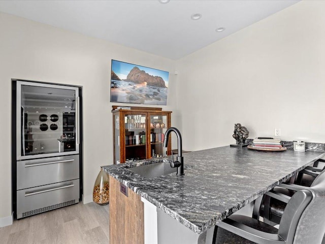 kitchen featuring dark stone counters, a kitchen bar, light wood-style floors, a warming drawer, and a sink