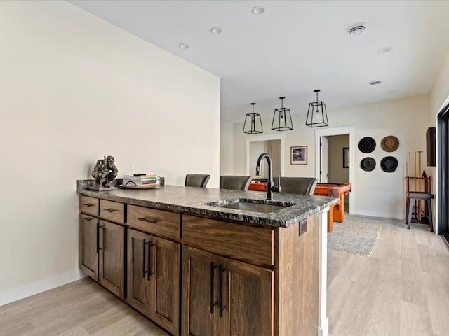 kitchen featuring a peninsula, baseboards, light wood finished floors, and a sink