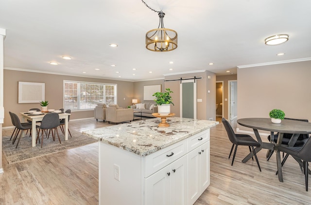 kitchen featuring light wood finished floors, a kitchen island, a barn door, hanging light fixtures, and white cabinetry