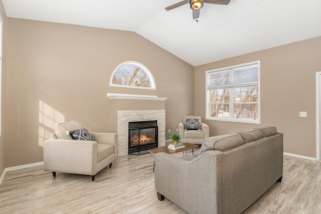 living room featuring a stone fireplace, vaulted ceiling, a healthy amount of sunlight, and light wood-style floors