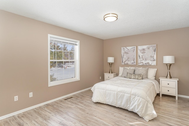 bedroom with visible vents, light wood-style flooring, a textured ceiling, and baseboards