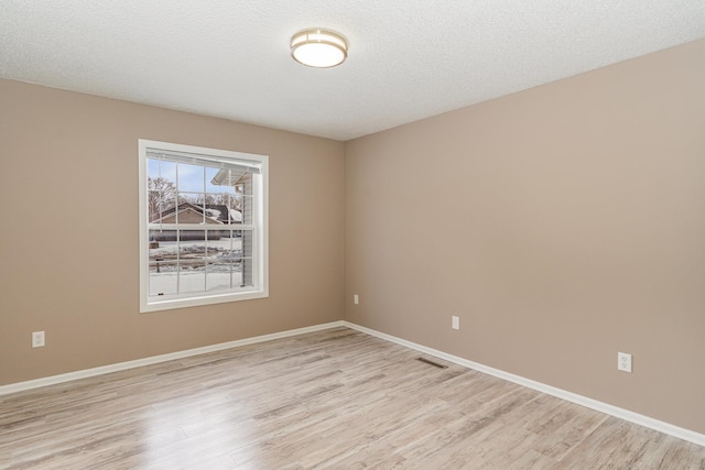 unfurnished room featuring visible vents, a textured ceiling, light wood-type flooring, and baseboards