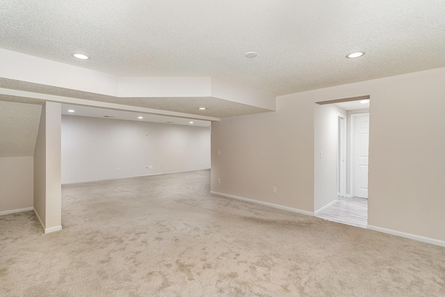 finished below grade area with light carpet, recessed lighting, a textured ceiling, and baseboards