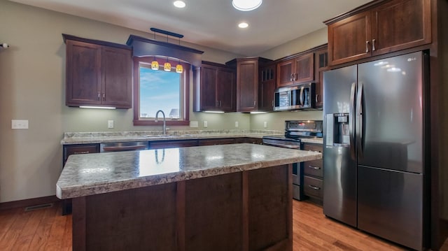 kitchen with a center island, light wood-style floors, hanging light fixtures, stainless steel appliances, and a sink