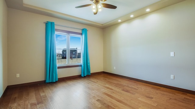 spare room featuring a tray ceiling, light wood-style floors, baseboards, and ceiling fan