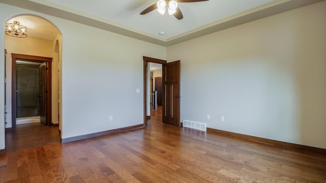 empty room with wood finished floors, visible vents, baseboards, arched walkways, and ceiling fan with notable chandelier