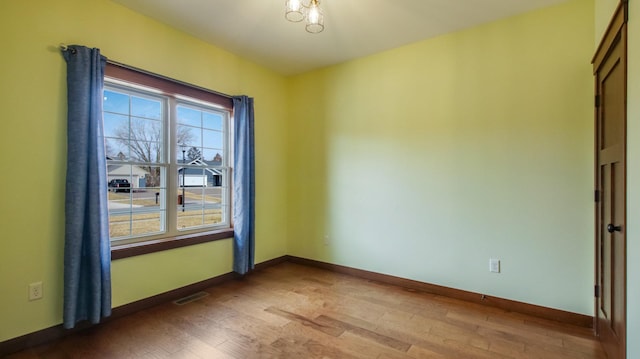 spare room featuring wood finished floors, visible vents, and baseboards