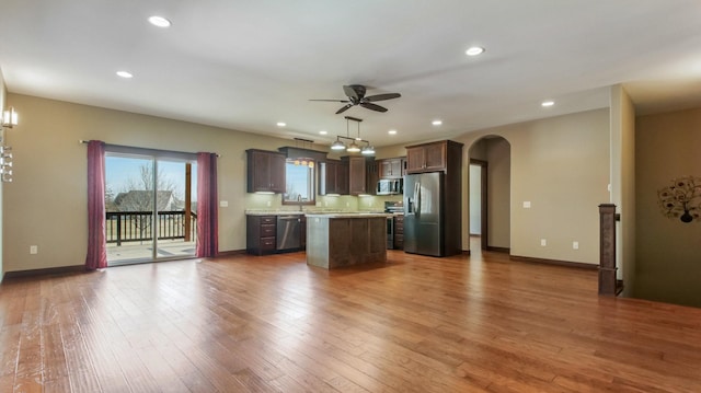 kitchen featuring a kitchen island, wood finished floors, stainless steel appliances, arched walkways, and light countertops