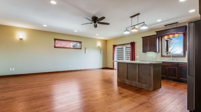 kitchen featuring dark brown cabinets, a center island, baseboards, a ceiling fan, and wood-type flooring