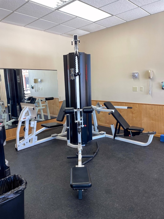 exercise room with a wainscoted wall, a paneled ceiling, and wood walls