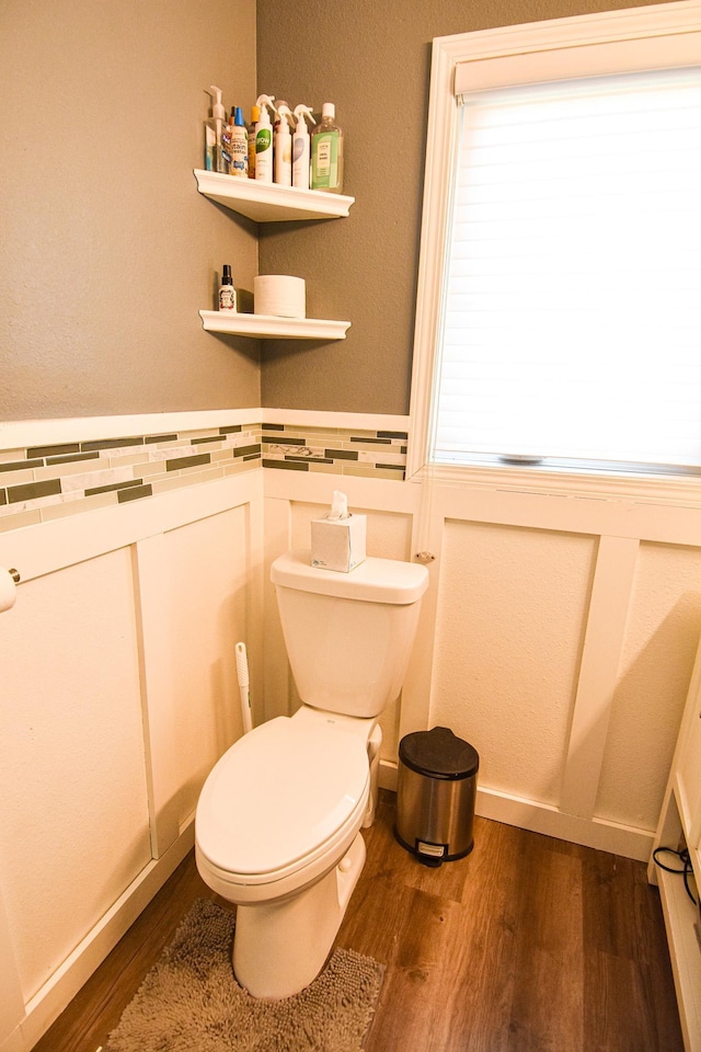 bathroom with toilet, wood finished floors, and a wainscoted wall