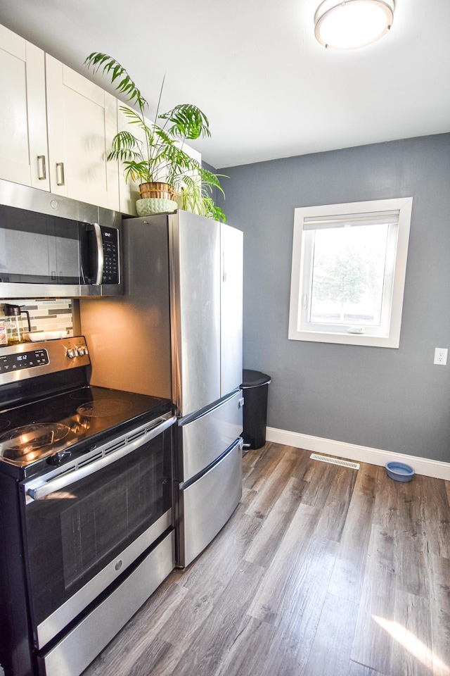 kitchen with wood finished floors, appliances with stainless steel finishes, white cabinets, decorative backsplash, and baseboards