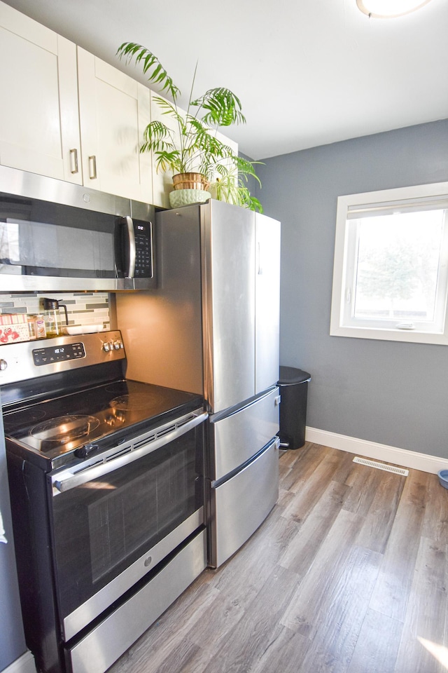 kitchen with tasteful backsplash, white cabinetry, appliances with stainless steel finishes, light wood finished floors, and baseboards