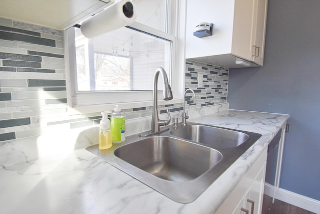 kitchen featuring a sink, baseboards, light stone counters, and tasteful backsplash