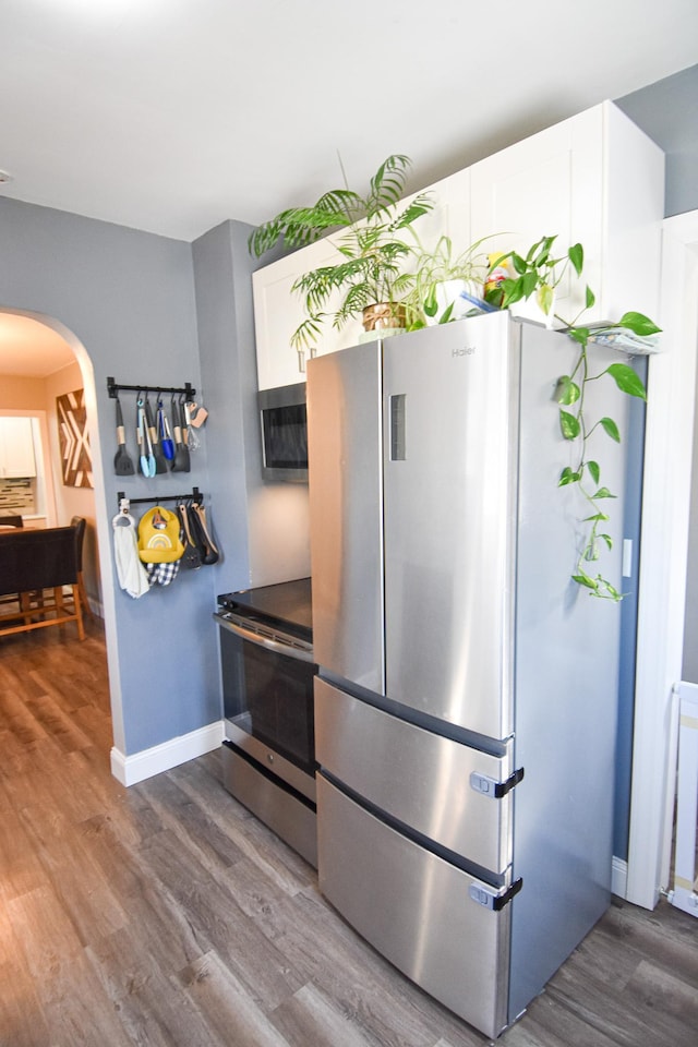 kitchen with baseboards, arched walkways, white cabinets, stainless steel appliances, and dark wood-style flooring