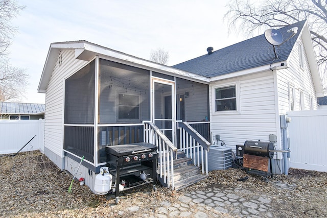 rear view of house with a shingled roof, fence, central AC, and a sunroom