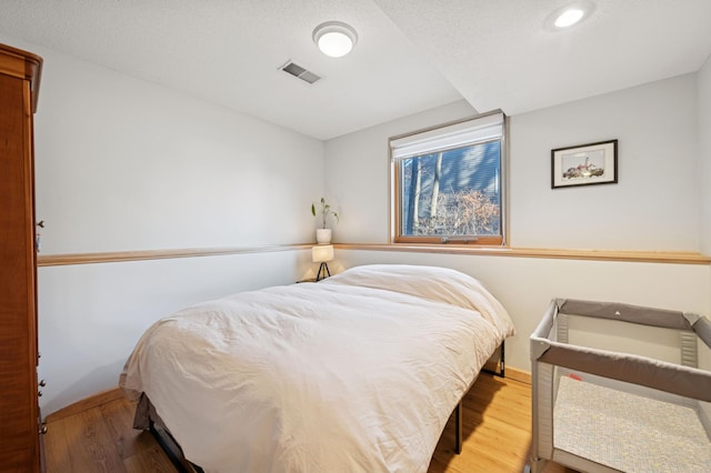 bedroom with visible vents, a textured ceiling, baseboards, and wood finished floors