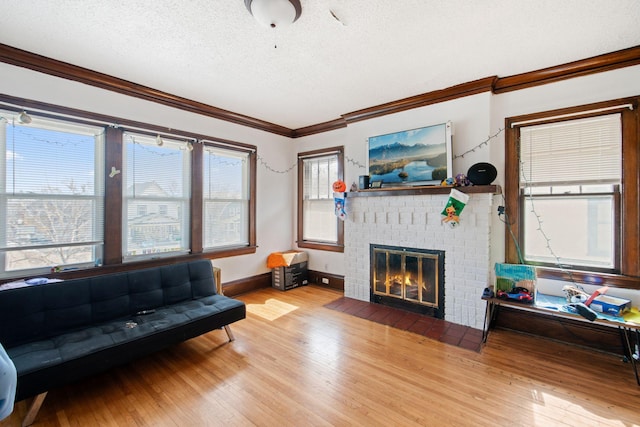 living room with wood finished floors, a fireplace, a textured ceiling, and ornamental molding