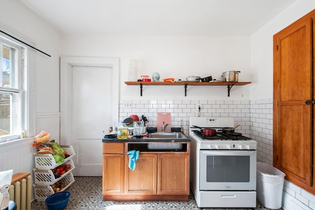 kitchen with brown cabinetry, a sink, white range with gas stovetop, and open shelves