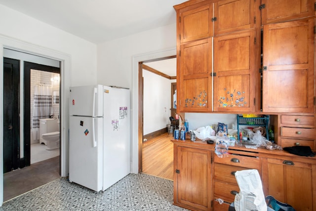 kitchen featuring light countertops, brown cabinetry, baseboards, and freestanding refrigerator