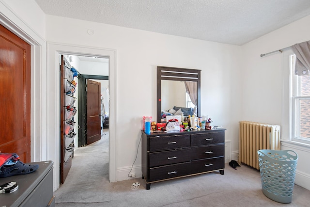 bedroom with light colored carpet, radiator, and a textured ceiling