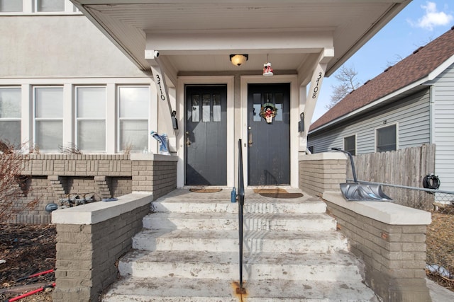 view of exterior entry with fence and stucco siding