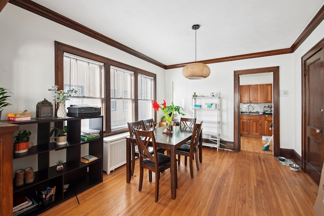 dining area featuring light wood-style flooring, radiator, crown molding, and baseboards