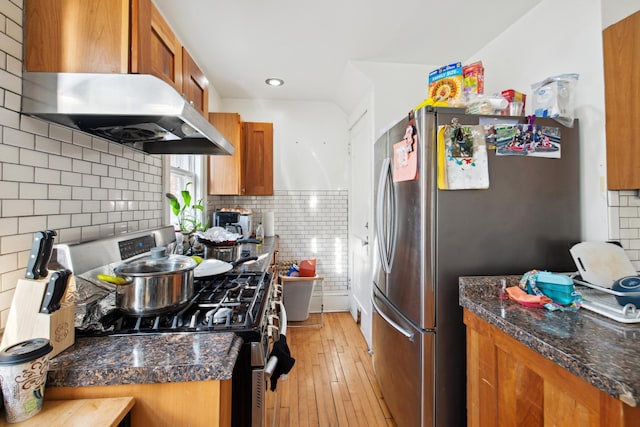 kitchen with ventilation hood, brown cabinetry, light wood-type flooring, and appliances with stainless steel finishes