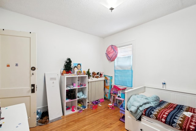 bedroom with a wainscoted wall, a textured ceiling, wood finished floors, and radiator