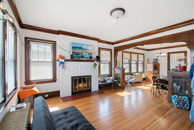 living room with a fireplace, wood finished floors, an inviting chandelier, and crown molding
