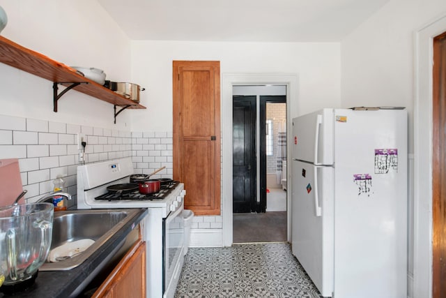 kitchen with white appliances, open shelves, brown cabinets, dark countertops, and a sink