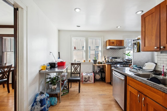 kitchen featuring tasteful backsplash, under cabinet range hood, dark countertops, dishwasher, and light wood-type flooring