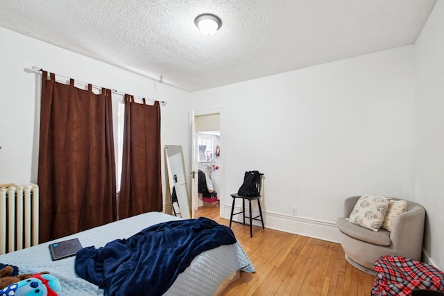 bedroom featuring radiator heating unit, baseboards, light wood-style flooring, and a textured ceiling
