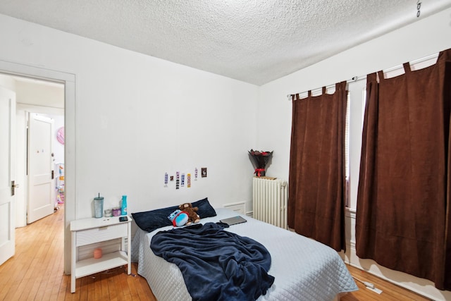 bedroom with radiator heating unit, a textured ceiling, and wood-type flooring