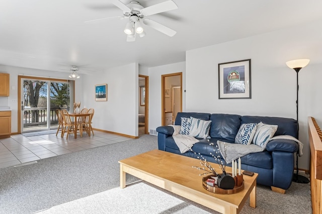 living room with baseboards, ceiling fan, light tile patterned flooring, and light colored carpet