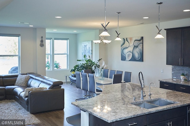 kitchen featuring dark wood-style floors, light stone countertops, a sink, decorative backsplash, and open floor plan