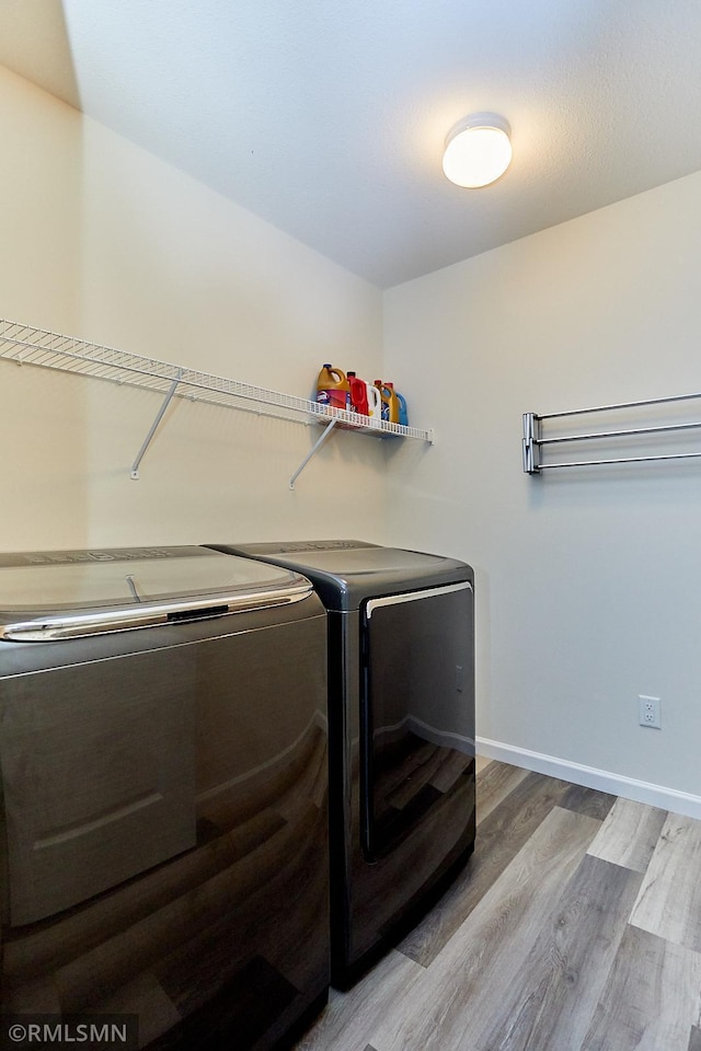 washroom featuring baseboards, wood finished floors, washing machine and dryer, and laundry area