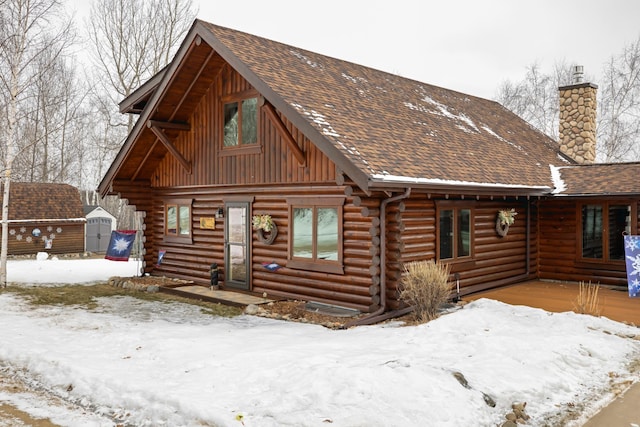 log-style house featuring log siding, a storage unit, an outdoor structure, and roof with shingles