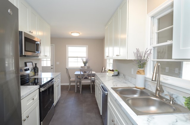 kitchen featuring a sink, stainless steel appliances, baseboards, and white cabinetry