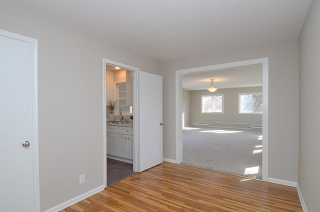 unfurnished room featuring a baseboard heating unit, baseboards, light wood finished floors, and a sink