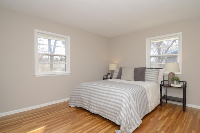 bedroom with baseboards, multiple windows, and light wood finished floors