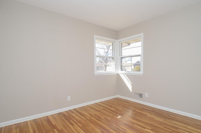 empty room with light wood finished floors, visible vents, and baseboards