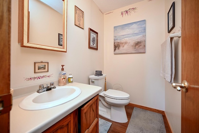 half bathroom featuring baseboards, toilet, wood finished floors, and vanity